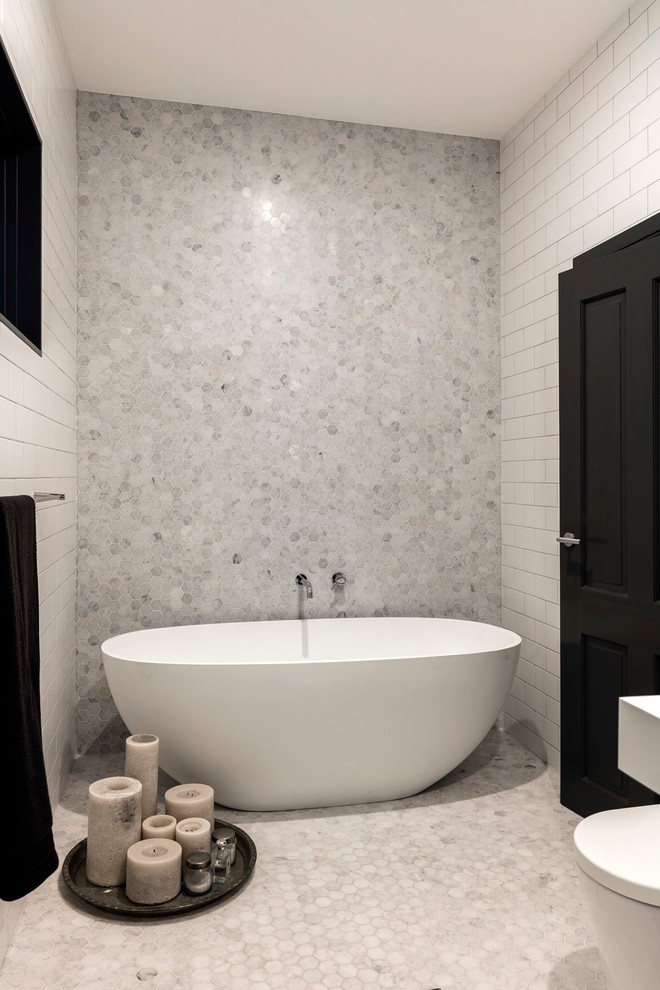 This is an example of a large traditional master bathroom in Sydney with recessed-panel cabinets, white cabinets, a freestanding tub, a wall-mount toilet, white tile, subway tile, white walls, marble floors, an integrated sink and engineered quartz benchtops.