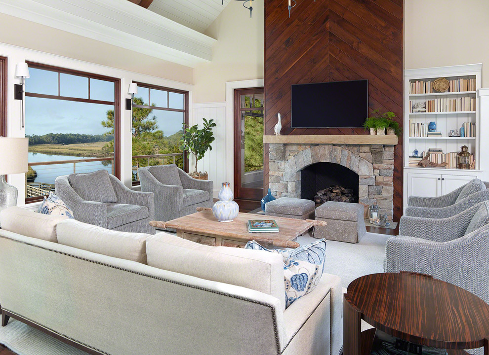 Photo of a large beach style family room in Charleston with beige walls, a standard fireplace, a stone fireplace surround, a wall-mounted tv and a library.