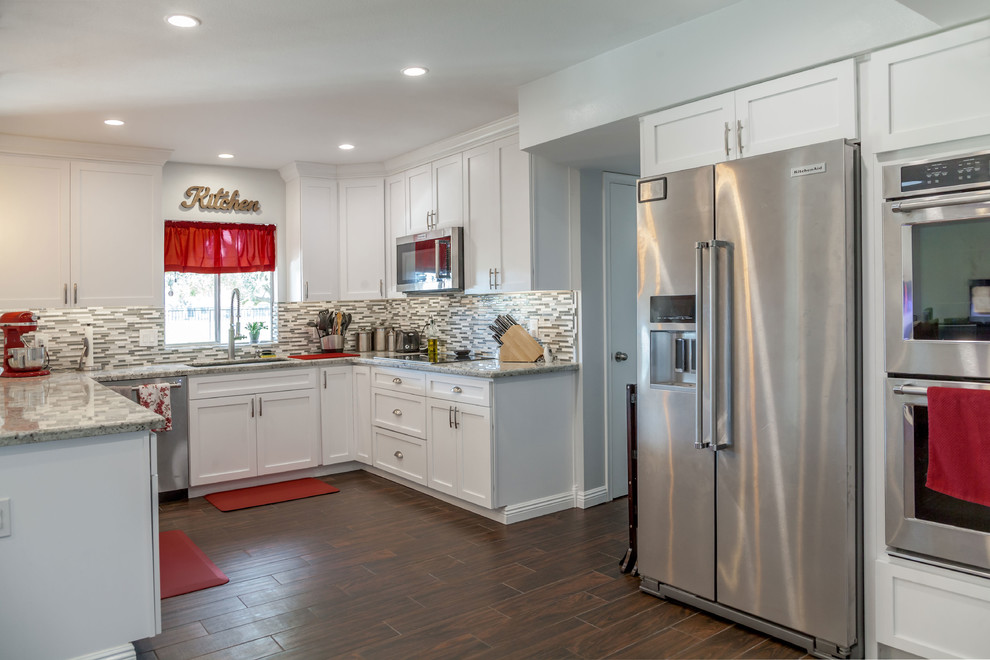 Example of a mid-sized transitional u-shaped laminate floor and brown floor open concept kitchen design in Phoenix with an undermount sink, recessed-panel cabinets, white cabinets, granite countertops, multicolored backsplash, mosaic tile backsplash and stainless steel appliances