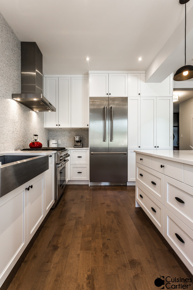 Inspiration for a mid-sized transitional l-shaped medium tone wood floor eat-in kitchen remodel in Montreal with a farmhouse sink, shaker cabinets, white cabinets, quartzite countertops, white backsplash, mosaic tile backsplash, stainless steel appliances and an island