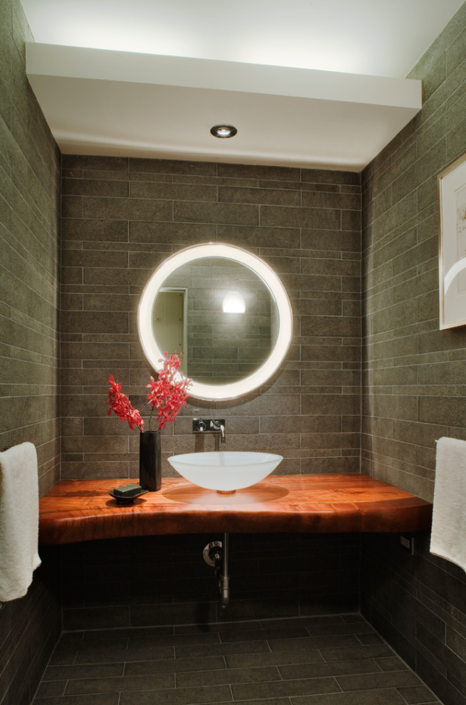 This is an example of a mid-sized asian powder room in New York with open cabinets, brown cabinets, a two-piece toilet, gray tile, stone tile, grey walls, slate floors, a vessel sink, wood benchtops, grey floor, brown benchtops, a floating vanity and recessed.