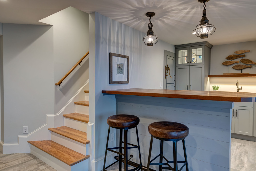 Mid-sized galley seated home bar in Boston with an undermount sink, shaker cabinets, blue cabinets, wood benchtops, porcelain floors, grey floor and brown benchtop.