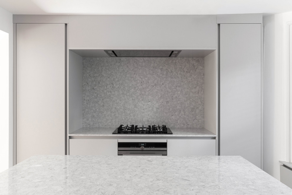 Modern inredning av ett avskilt, stort grå grått u-kök, med en integrerad diskho, släta luckor, grå skåp, bänkskiva i kvarts, grått stänkskydd, stänkskydd i sten, integrerade vitvaror, klinkergolv i porslin, en köksö och grått golv