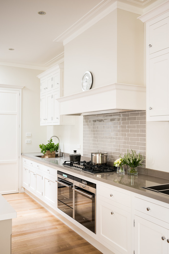 Design ideas for a traditional kitchen in Melbourne with a drop-in sink, recessed-panel cabinets, white cabinets, granite benchtops, stainless steel appliances, light hardwood floors and with island.