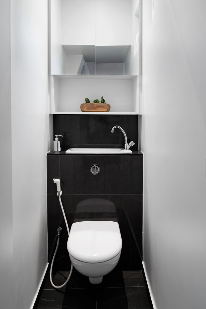 This is an example of a small contemporary powder room in Paris with beaded inset cabinets, a wall-mount toilet, white walls, marble floors, an integrated sink, tile benchtops and black floor.