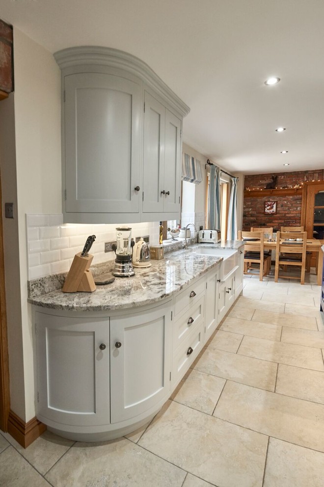 This is an example of a large contemporary eat-in kitchen in Other with a farmhouse sink, shaker cabinets, grey cabinets, granite benchtops, white splashback, ceramic splashback, stainless steel appliances, travertine floors and with island.
