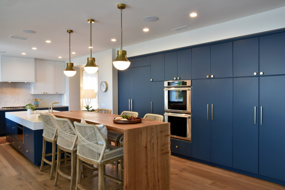 Large modern u-shaped eat-in kitchen in San Diego with a double-bowl sink, flat-panel cabinets, blue cabinets, quartzite benchtops, white splashback, ceramic splashback, panelled appliances, medium hardwood floors, with island, brown floor and grey benchtop.