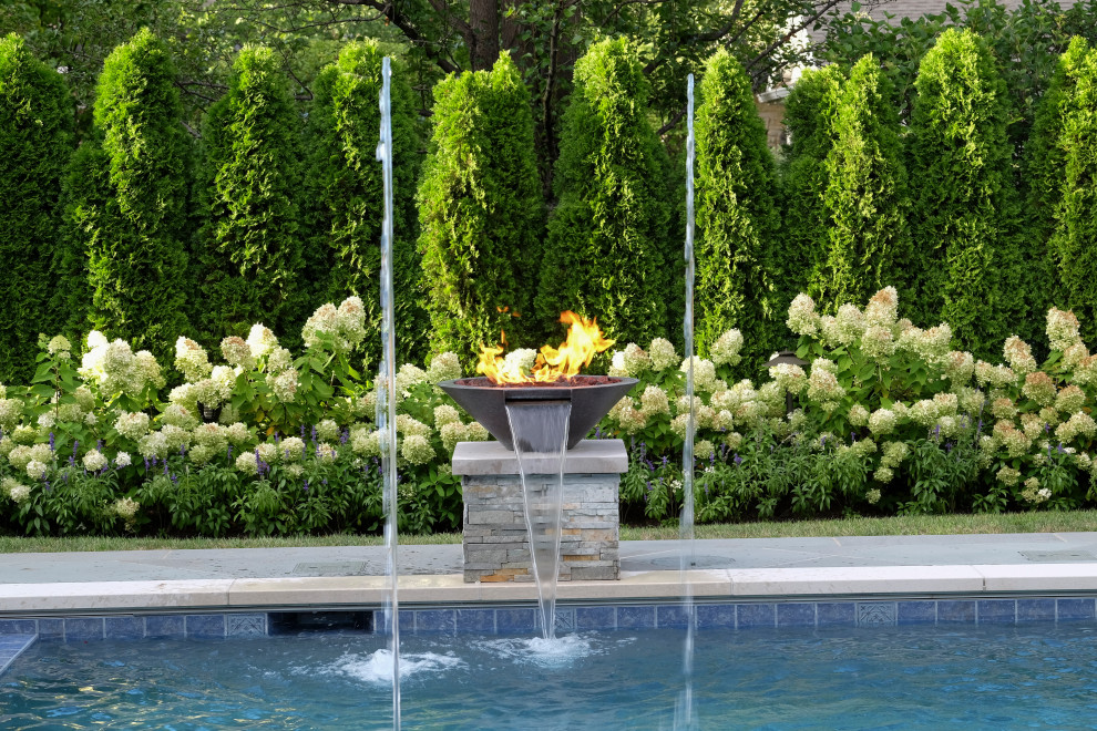 Ejemplo de piscina alargada clásica de tamaño medio rectangular en patio trasero con privacidad y adoquines de piedra natural