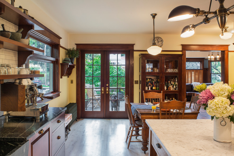 Expansive arts and crafts l-shaped eat-in kitchen in Portland with an integrated sink, raised-panel cabinets, medium wood cabinets, soapstone benchtops, white splashback, subway tile splashback, black appliances, light hardwood floors and with island.