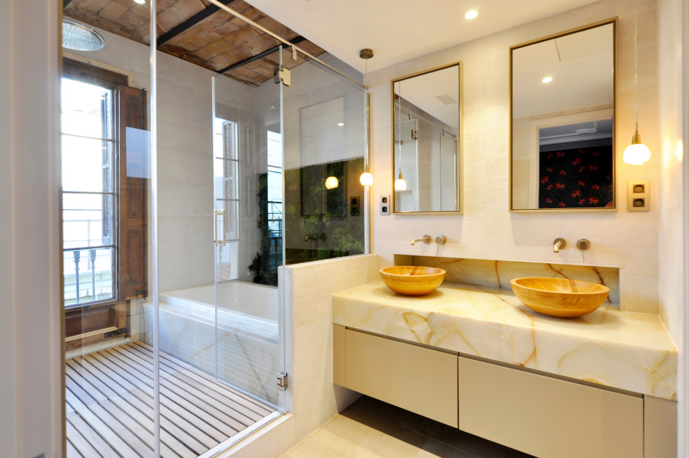 Photo of a large modern master bathroom in Barcelona with flat-panel cabinets, beige cabinets, a drop-in tub, a shower/bathtub combo, a one-piece toilet, white tile, ceramic tile, white walls, ceramic floors, a vessel sink, onyx benchtops, white floor, a hinged shower door, multi-coloured benchtops, an enclosed toilet, a double vanity and a built-in vanity.