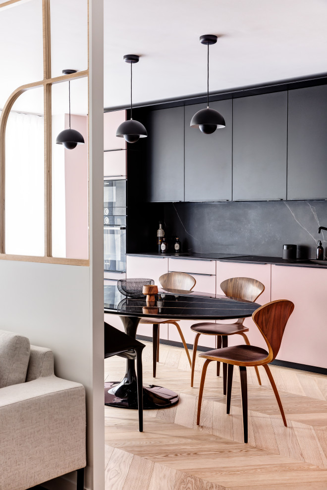Пример оригинального дизайна: прямая кухня-гостиная среднего размера в стиле модернизм с врезной мойкой, плоскими фасадами, розовыми фасадами, черным фартуком, черной техникой, светлым паркетным полом, коричневым полом, черной столешницей и двухцветным гарнитуром без острова