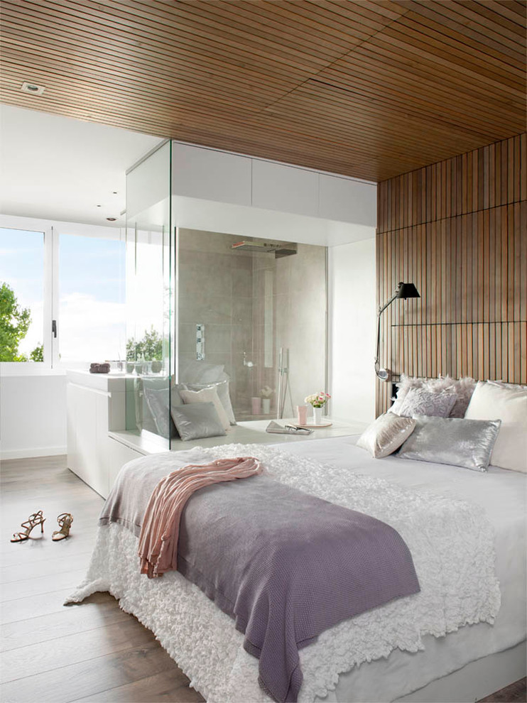 This is an example of a modern master bedroom in New York with white walls and medium hardwood floors.