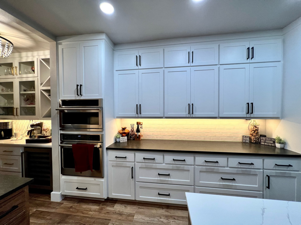 Example of a huge u-shaped vinyl floor, multicolored floor and vaulted ceiling eat-in kitchen design with an undermount sink, shaker cabinets, white cabinets, quartz countertops, beige backsplash, glass tile backsplash, stainless steel appliances, an island and multicolored countertops