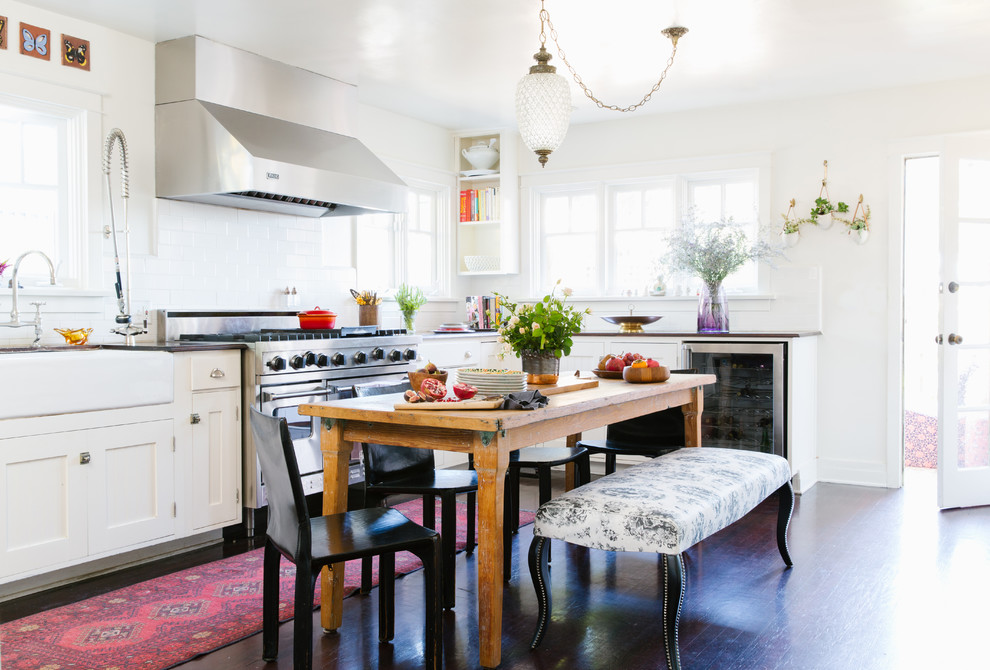 Eclectic l-shaped eat-in kitchen in Los Angeles with a farmhouse sink, recessed-panel cabinets, white cabinets, wood benchtops, white splashback, stainless steel appliances, no island, subway tile splashback and dark hardwood floors.