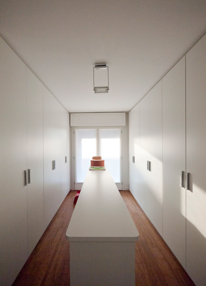 Photo of a large modern gender-neutral walk-in wardrobe in Milan with flat-panel cabinets, white cabinets and bamboo floors.