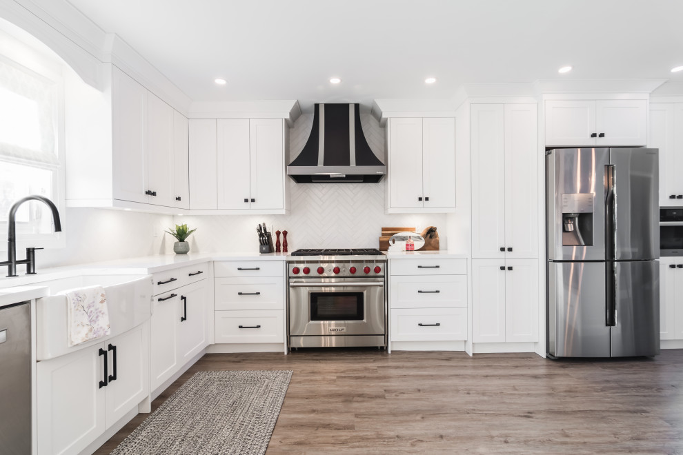 Transitional l-shaped medium tone wood floor and brown floor kitchen photo in Toronto with a farmhouse sink, shaker cabinets, white cabinets, white backsplash, stainless steel appliances, no island and white countertops