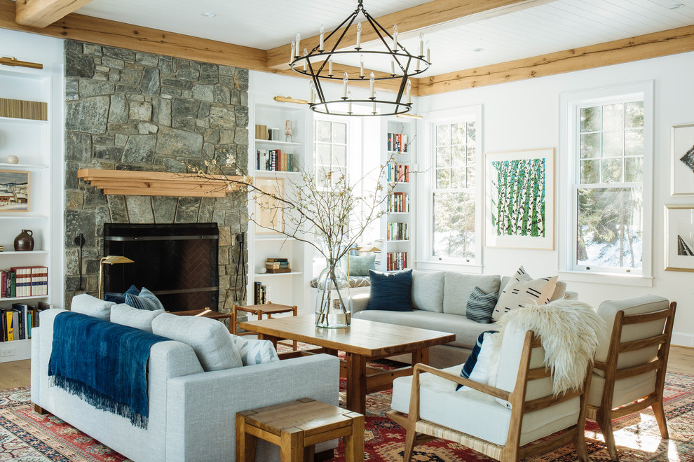 This is an example of a large transitional formal open concept living room in Portland Maine with white walls, light hardwood floors, a standard fireplace, a stone fireplace surround, no tv and brown floor.