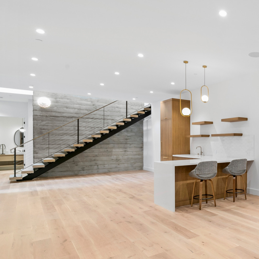 Design ideas for a mid-sized midcentury l-shaped seated home bar in San Francisco with an undermount sink, flat-panel cabinets, light wood cabinets, solid surface benchtops, white splashback, porcelain splashback, light hardwood floors, brown floor and white benchtop.