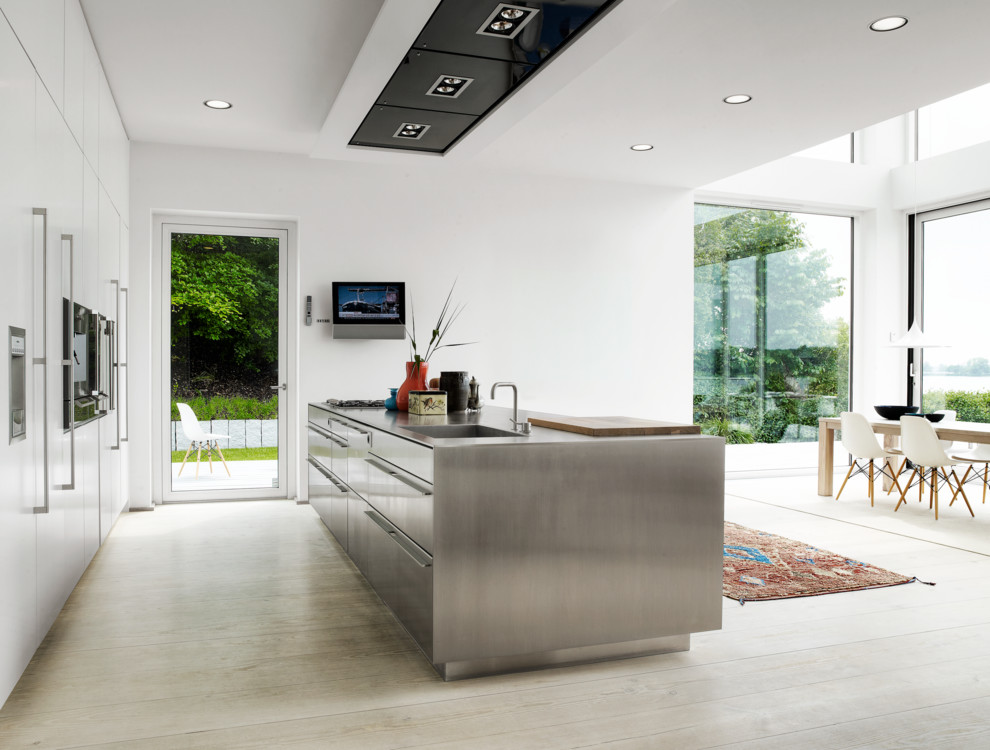 Photo of a large scandinavian single-wall open plan kitchen in Aarhus with a single-bowl sink, flat-panel cabinets, white cabinets, stainless steel benchtops, stainless steel appliances, light hardwood floors, with island and beige floor.