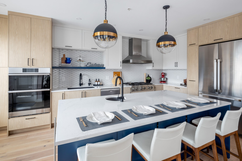 This is an example of a large contemporary l-shaped open plan kitchen in Vancouver with flat-panel cabinets, light wood cabinets, engineered stone countertops, white splashback, ceramic splashback, stainless steel appliances, an island and white worktops.
