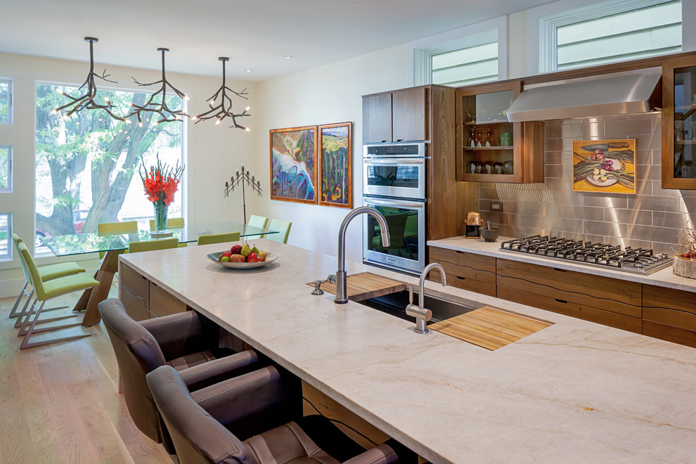 This is an example of a contemporary galley eat-in kitchen in Chicago with an undermount sink, flat-panel cabinets, medium wood cabinets, metallic splashback, metal splashback, stainless steel appliances, marble benchtops, medium hardwood floors and beige benchtop.