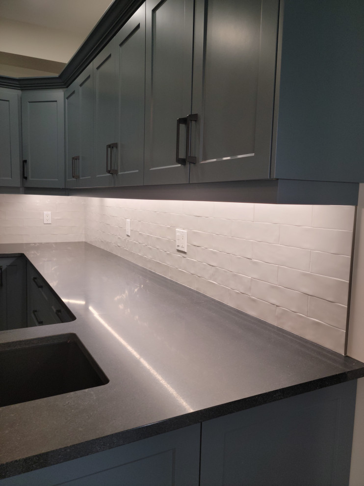 Mid-sized transitional u-shaped vinyl floor eat-in kitchen photo with an undermount sink, recessed-panel cabinets, blue cabinets, quartzite countertops, white backsplash, porcelain backsplash, black appliances, a peninsula and black countertops