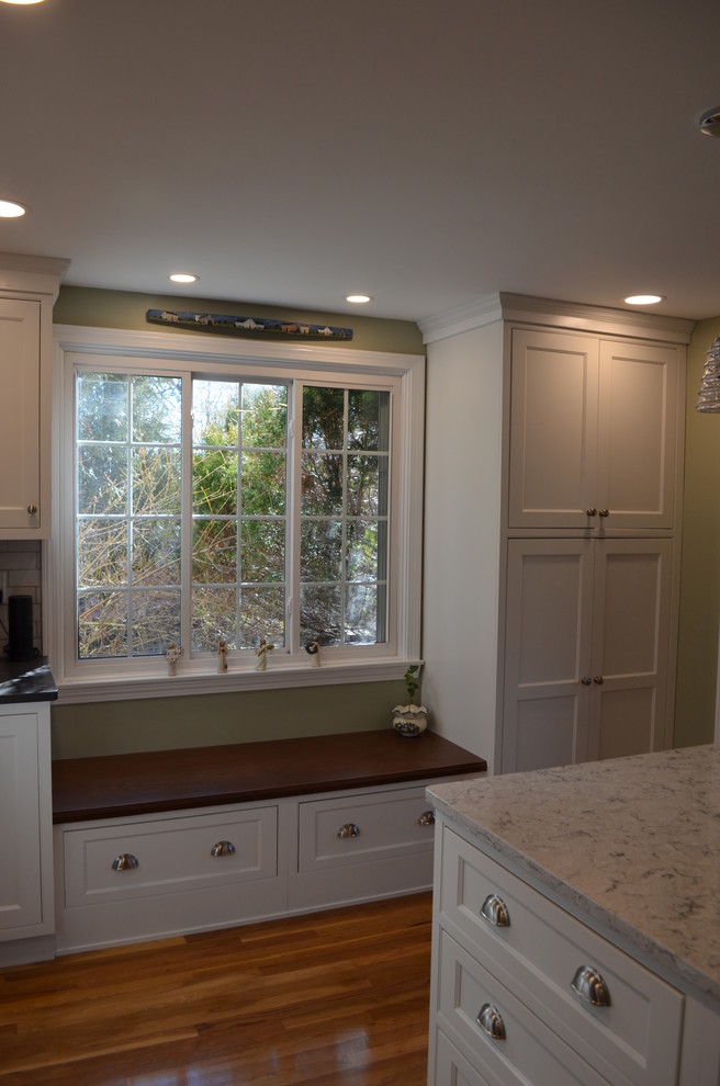 Transitional l-shaped light wood floor eat-in kitchen photo in Boston with an undermount sink, beaded inset cabinets, white cabinets, quartz countertops, white backsplash, ceramic backsplash, stainless steel appliances, an island and gray countertops