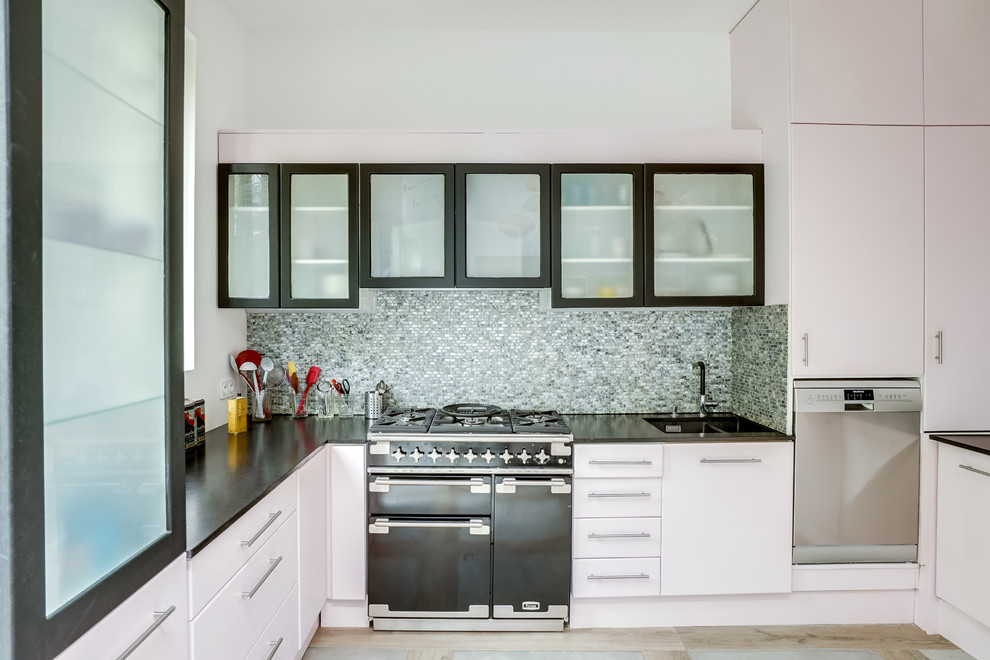 Photo of a large industrial u-shaped open plan kitchen in Paris with an undermount sink, flat-panel cabinets, granite benchtops, multi-coloured splashback, mosaic tile splashback, black appliances, ceramic floors, with island, grey floor and black benchtop.