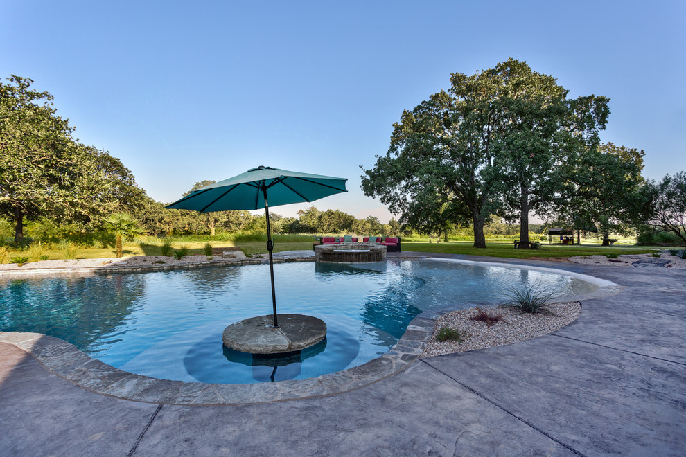 Inspiration for an expansive arts and crafts backyard custom-shaped pool in Dallas with a hot tub and stamped concrete.