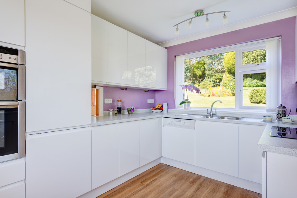 Design ideas for a small contemporary u-shaped separate kitchen in Devon with a double-bowl sink, flat-panel cabinets, white cabinets, laminate benchtops, multi-coloured splashback, stainless steel appliances and medium hardwood floors.