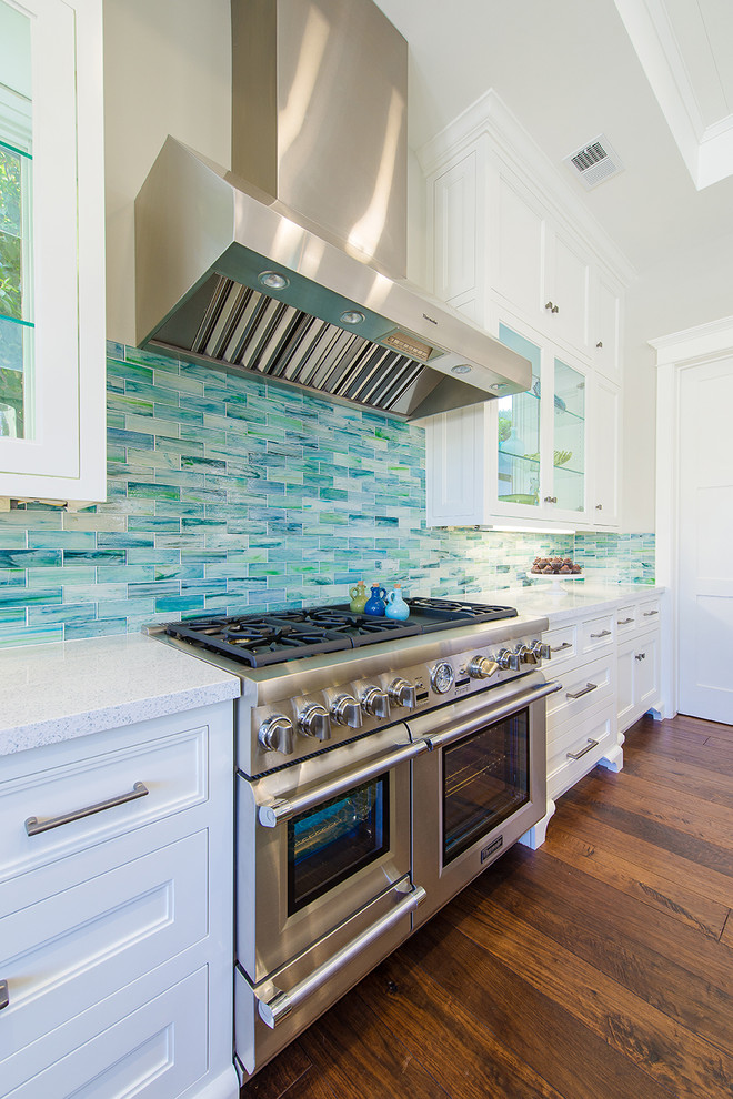 Beach style u-shaped medium tone wood floor eat-in kitchen photo in Los Angeles with an integrated sink, recessed-panel cabinets, white cabinets, quartz countertops, multicolored backsplash, mosaic tile backsplash, stainless steel appliances and an island