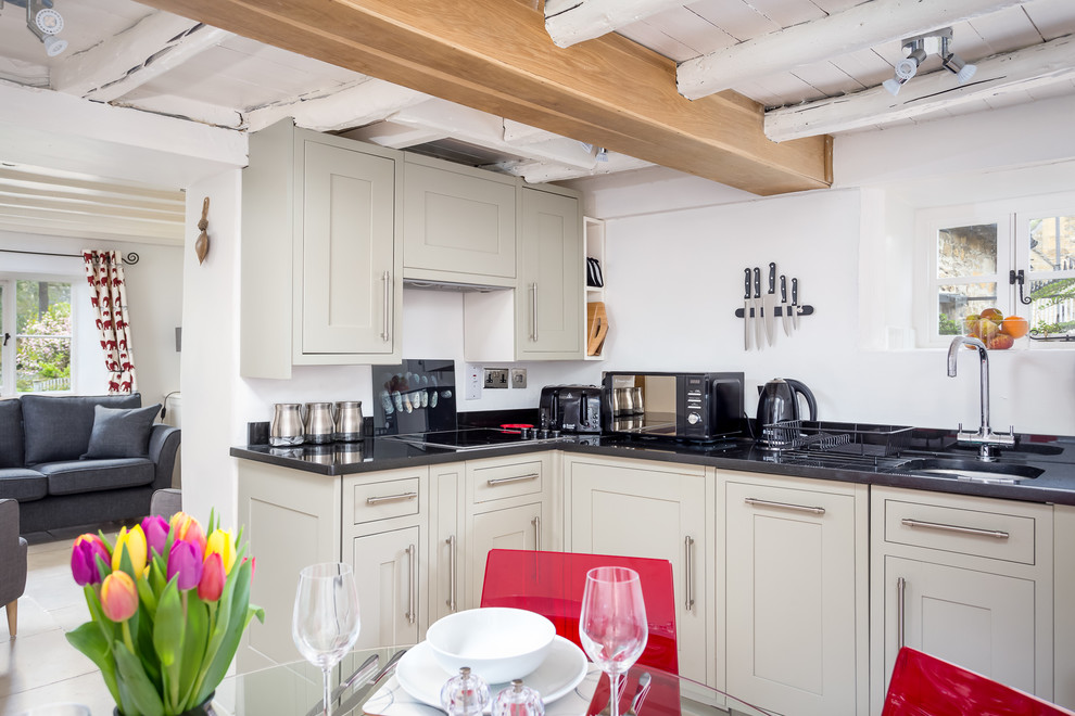 Photo of a small country l-shaped eat-in kitchen in Gloucestershire with an undermount sink, shaker cabinets, granite benchtops, black splashback, glass sheet splashback and black appliances.