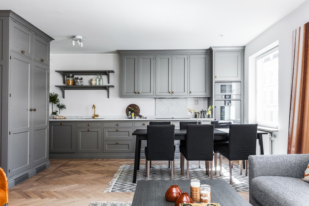 Inspiration for a scandinavian l-shaped open plan kitchen in Stockholm with an undermount sink, shaker cabinets, grey cabinets, panelled appliances, light hardwood floors, no island and marble benchtops.