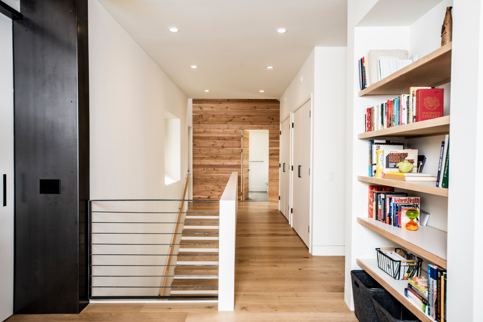 Photo of a mid-sized contemporary hallway with white walls, light hardwood floors, white floor and wood walls.