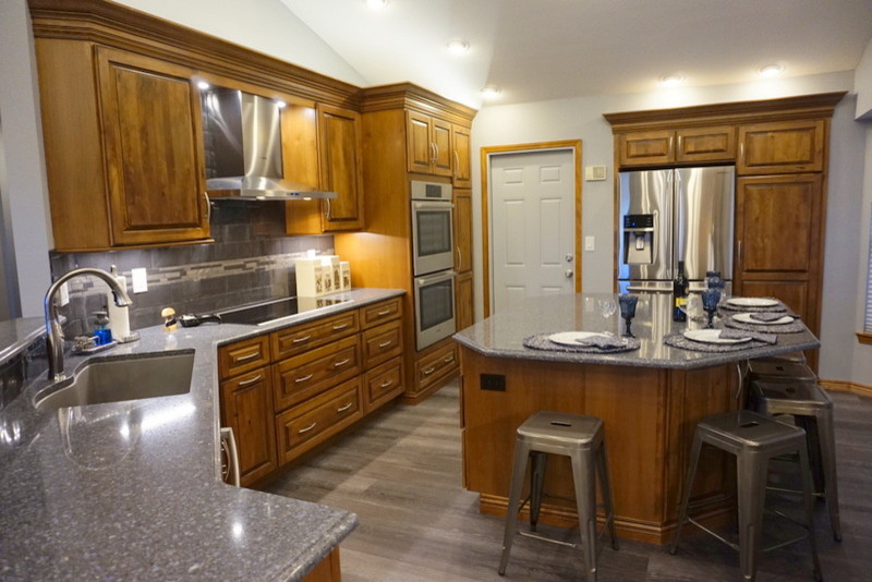 Eat-in kitchen - large rustic gray floor eat-in kitchen idea with an undermount sink, raised-panel cabinets, medium tone wood cabinets, quartz countertops, gray backsplash, metal backsplash, stainless steel appliances and an island