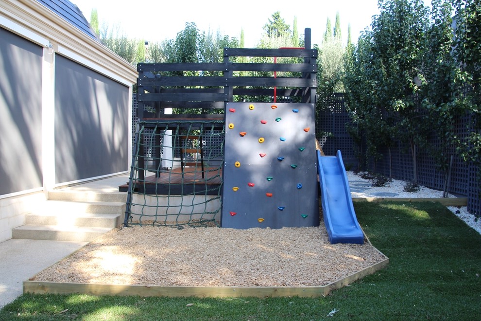 Photo of a mid-sized contemporary backyard partial sun formal garden for spring in Melbourne with with outdoor playset and mulch.