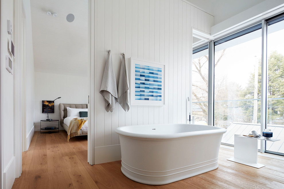 This is an example of a contemporary master bathroom in Vancouver with a freestanding tub, white walls, medium hardwood floors and brown floor.