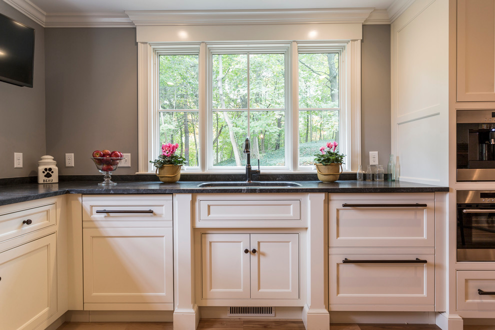 Inspiration for a large transitional l-shaped eat-in kitchen in Boston with an undermount sink, shaker cabinets, white cabinets, stainless steel appliances, light hardwood floors and with island.
