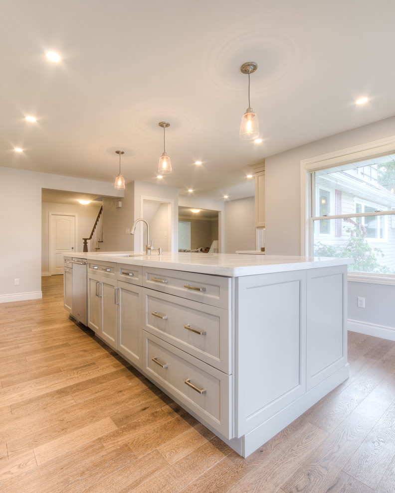 Open concept kitchen - mid-sized transitional galley light wood floor and beige floor open concept kitchen idea in Toronto with a double-bowl sink, recessed-panel cabinets, white cabinets, solid surface countertops, white backsplash, porcelain backsplash, stainless steel appliances, an island and white countertops