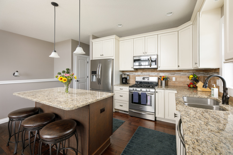 Inspiration for a mid-sized transitional l-shaped medium tone wood floor, brown floor and vaulted ceiling eat-in kitchen remodel with an undermount sink, flat-panel cabinets, white cabinets, granite countertops, beige backsplash, stone tile backsplash, stainless steel appliances, an island and beige countertops