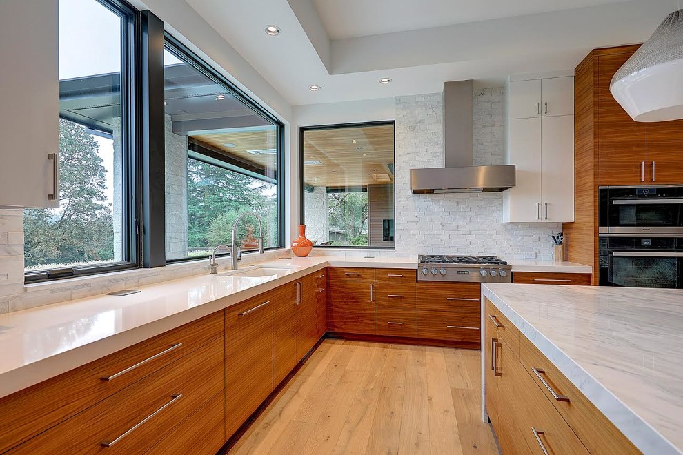 Photo of a large contemporary u-shaped eat-in kitchen in Portland with an undermount sink, flat-panel cabinets, medium wood cabinets, marble benchtops, white splashback, stone tile splashback, stainless steel appliances, light hardwood floors, with island, beige floor and white benchtop.