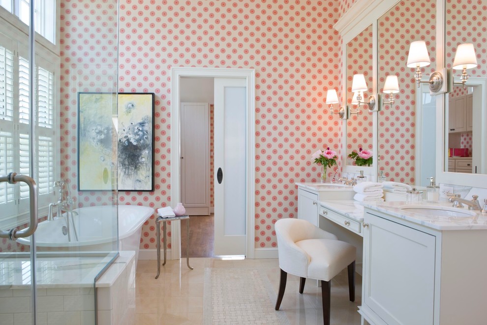 Photo of a large beach style master bathroom in Boston with an undermount sink, recessed-panel cabinets, white cabinets, marble benchtops, a freestanding tub, a corner shower, beige tile, stone tile, pink walls and porcelain floors.