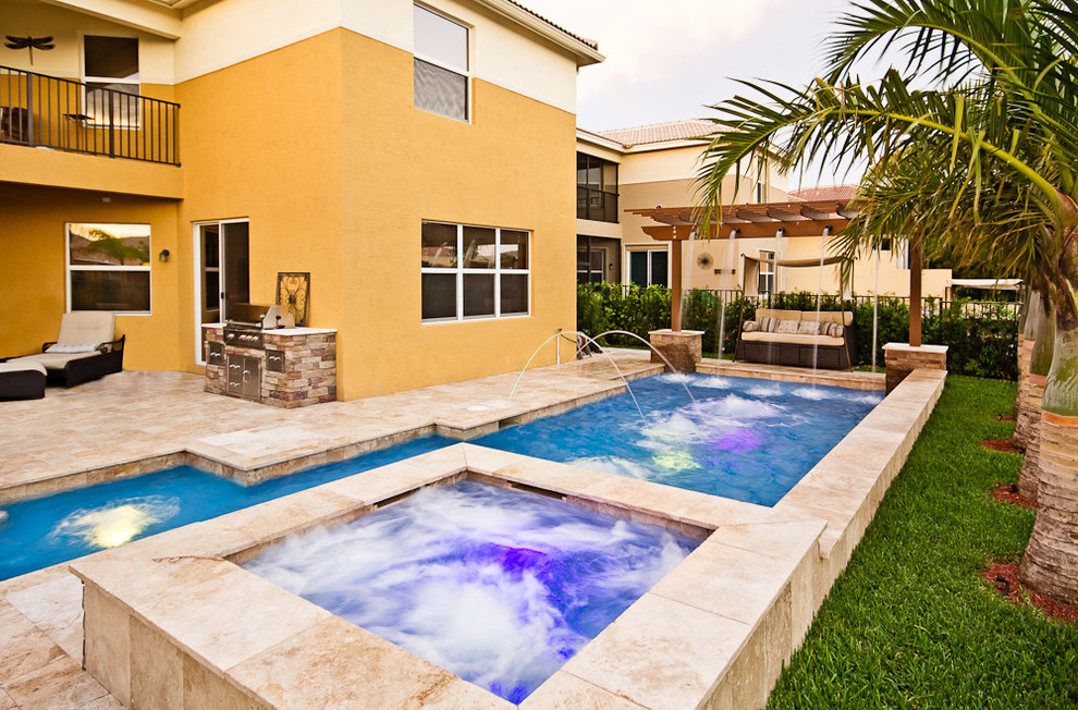 Design ideas for a large mediterranean backyard custom-shaped lap pool in Miami with a water feature and natural stone pavers.