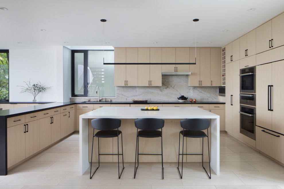 Inspiration for a medium sized contemporary u-shaped open plan kitchen in San Francisco with flat-panel cabinets, light wood cabinets, white splashback, stone slab splashback, integrated appliances, an island, beige floors, black worktops, a submerged sink, engineered stone countertops and limestone flooring.