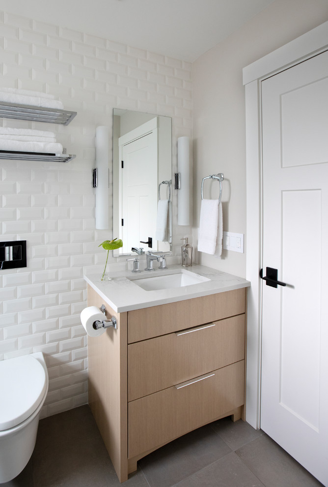 This is an example of a mid-sized arts and crafts 3/4 bathroom in Vancouver with white cabinets, an alcove tub, a shower/bathtub combo, a wall-mount toilet, white tile, ceramic tile, white walls, porcelain floors, an undermount sink, engineered quartz benchtops, grey floor, a hinged shower door, white benchtops and flat-panel cabinets.
