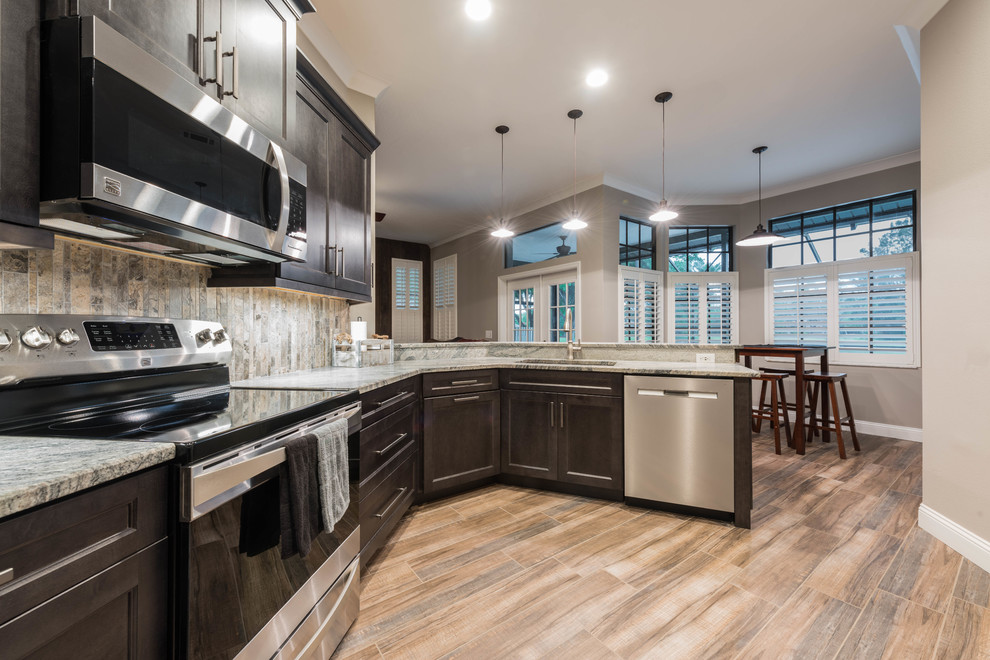 Large transitional l-shaped porcelain tile and brown floor eat-in kitchen photo in Orlando with shaker cabinets, gray cabinets, granite countertops, multicolored backsplash, travertine backsplash, stainless steel appliances, a peninsula and multicolored countertops