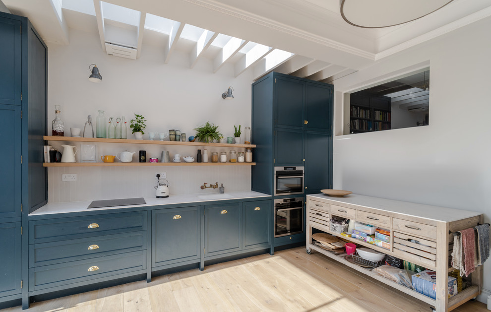 Transitional single-wall kitchen in London with shaker cabinets, blue cabinets, light hardwood floors, no island, beige floor and white benchtop.