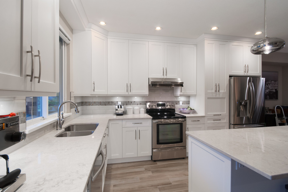 Inspiration for a mid-sized transitional l-shaped light wood floor eat-in kitchen remodel in Vancouver with an undermount sink, shaker cabinets, white cabinets, quartz countertops, white backsplash, ceramic backsplash, stainless steel appliances and an island