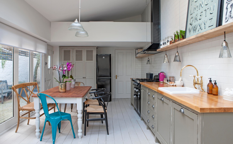 Inspiration for a traditional single-wall eat-in kitchen in London with a drop-in sink, shaker cabinets, grey cabinets, wood benchtops, white splashback, subway tile splashback, black appliances, painted wood floors, no island, white floor, brown benchtop and vaulted.