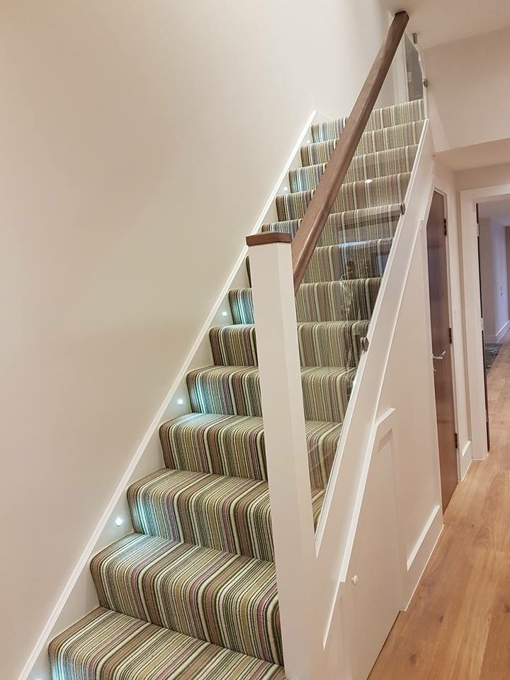 Large modern carpeted l-shaped staircase in London with carpet risers and glass railing.